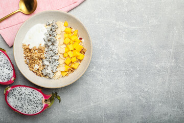 Bowl of granola with pitahaya, mango and yogurt served on light grey table, flat lay. Space for text