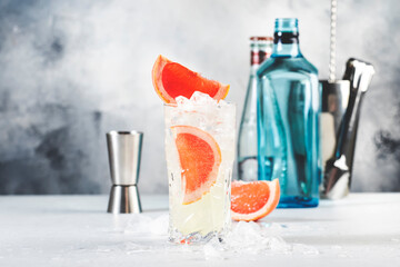 Gin bitter lemon trendy alcoholic cocktail drink with dry gin, tonic, grapefruit and ice cubes, bar tools. Gray background with copy space
