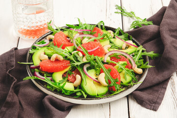 Healthy vegan vegetarian lunch salad with arugula, avocado, grapefruit and cashews and dressing of olive oil, honey and wine vinegar. White rustic kitchen table, top view