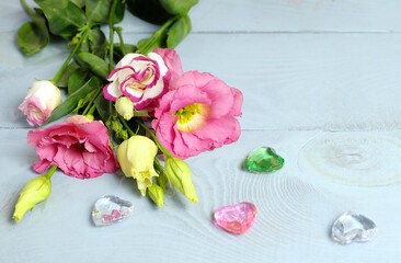 Blooming lisianthus (eustoma) and glass hearts on a blue wooden table, horizontal composition for Valentine's Day, Women's Day, etc., selective focus.