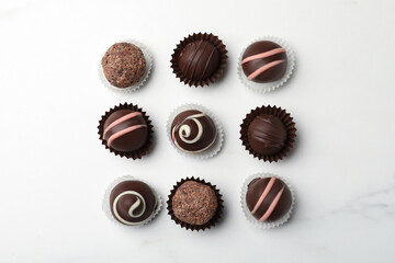 Different delicious chocolate truffles on white marble table, flat lay
