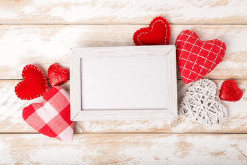 Photo frame between Valentines day romantic decoration with hearts and chocolate on a white wooden table. Top view, copy space.
