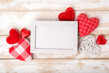 Photo frame between Valentines day romantic decoration with hearts and chocolate on a white wooden table. Top view, copy space.