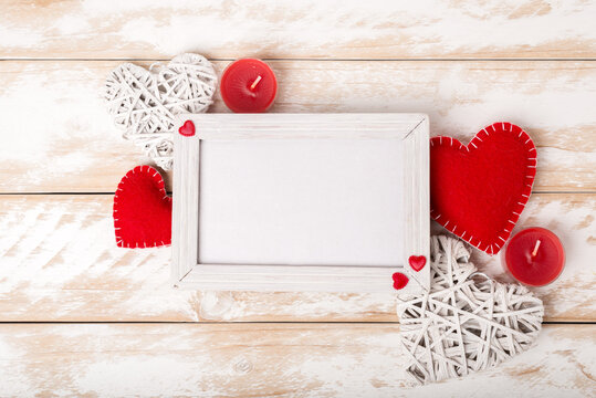 Photo frame between Valentines day romantic decoration with heart and candle on a white wooden table. Top view, copy space.