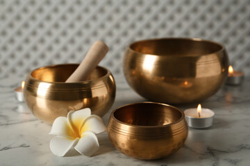 Tibetan singing bowls, mallet, plumeria flower and burning candles on white marble table