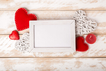 Photo frame between Valentines day romantic decoration with hearts, candle and chocolate on a white wooden table. Top view, copy space.