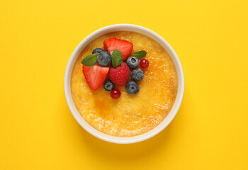 Delicious creme brulee with fresh berries on yellow background, top view