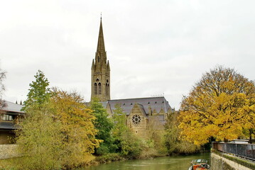 Fototapeta na wymiar Church with a steeple, surrounded by autumn foliage, on the bank of the River Avon in Bath, England