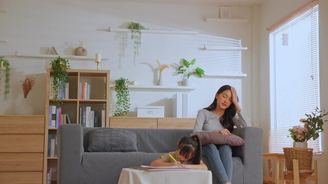 Children education. Lovely beautiful Asian single mom vacuuming the floor while the little cute daughter sits at Japanese table doing homework. Child care and motherhood duties at home concept.