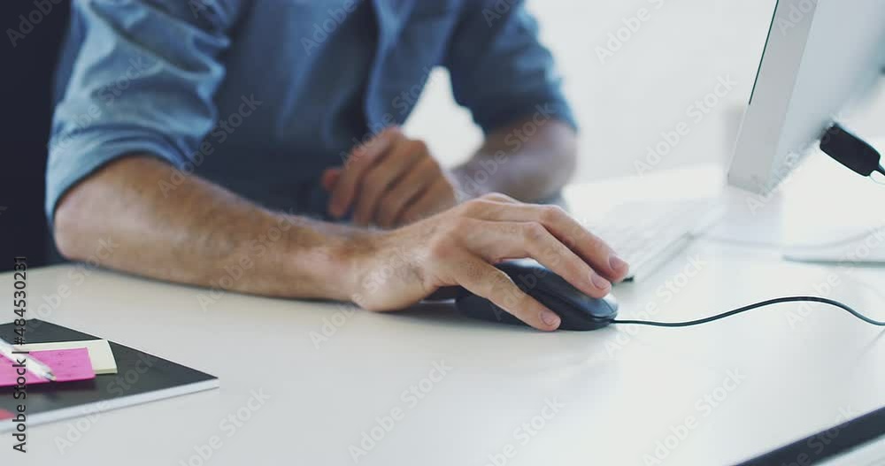 Poster Design in focus. Man working on a computer in a modern office. One unknown businessman clicking a mouse using a computer at a desk in an office at work.