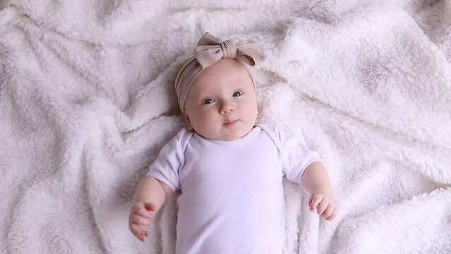Top view portrait of a cute newborn three month old baby girl lying on her back on a white blanket and looking at the camera. The concept of childhood, new life, motherhood,