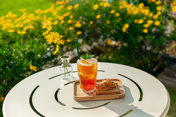 fresh homemade peach ice tea with mint, chocolate chip cookie served on table outdoors. summer cold fruit drink in sunny afternoon with yellow flowers behind