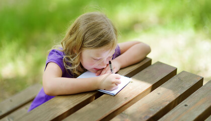 Little girl drawing at the wooden table outdoors. Little kid sketching outside on beautiful summer day.