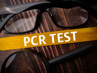 Top view padlock and calcuator with brown card with text PCR TEST on wooden background.