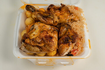 Portuguese Peri Peri Chicken on top of rice and potato balls  in a styrofoam dish 