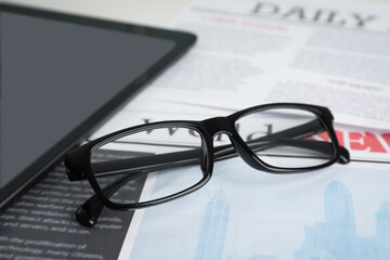 Glasses and tablet on newspaper, closeup view
