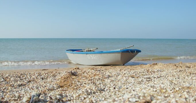 Old empty blue grey boat arrived ashore lying on beach wet soft sand and washed by rolling sea waves under clear sky ON sunny day