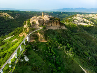 Aerial summer evening view of famous Civita di Bagnoregio town, beautiful place located on top of a volcanic tuff hill overlooking the Tiber river valley - obrazy, fototapety, plakaty