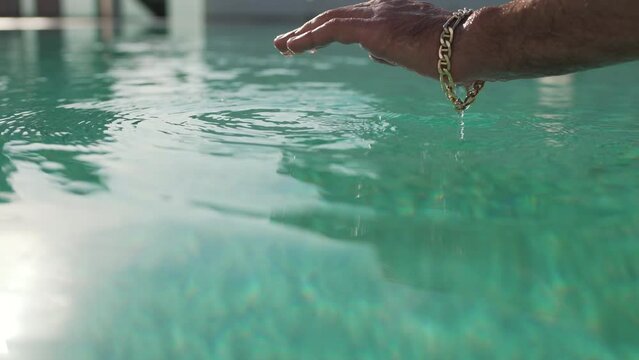 a man with a bracelet on his wrist dips his hand into the pool