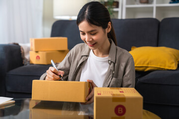 Fototapeta na wymiar Startup small business concept, young woman owner working and packing on the box to customer at home office, seller prepares the delivery.