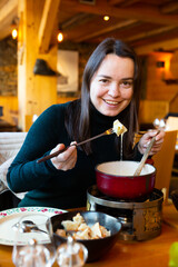 Portrait of cheerful woman eating traditional Swiss cheese fondue
