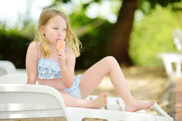 Cute young girl in a swimsuit having an ice cream by outdoor pool. Child having fun on hot summer day. Kid eating gelato on family vacations in Italy.