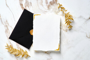 Luxury wedding invitation card mockup with black envelope and golden leaves on marble gold table. Flat lay, top view. Elegant wedding stationery set.