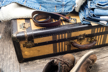 denim jacket, worn boots, a belt and a stack of blue jeans lie on a vintage suitcase. The concept of travel and comfortable equipment.