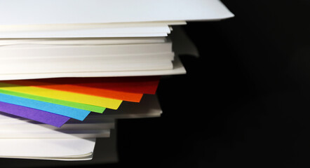 gay lesbian bisexual queer transgender community rainbow flag colors poking out of a ream of crisp white office paper on a plain black background. Gender idenity and diversity concept.