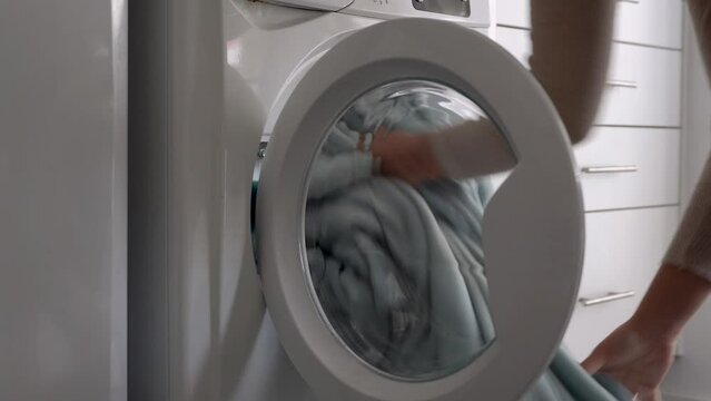 Female put blanket into laundry machine, Load clothes to washer machine and close door.