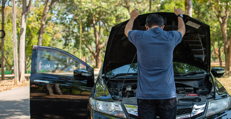 Man stands and inspects a broken-down car in a rural suburban forest. Black car, Engine won't...