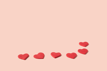 Pattern of red hearts made from modeling clay on a pastel pink background with copy space