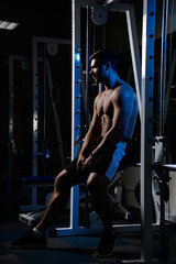 Muscular athletic young man fitness model resting after exercises in gym