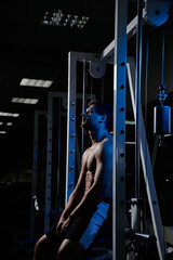 Muscular athletic young man fitness model resting after exercises in gym