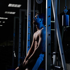 Muscular athletic young man fitness model resting after exercises in gym