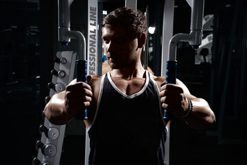 Muscular athletic young man fitness model do exercises in gym