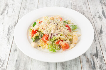 Caesar salad with chicken. In a white plate. Light wooden background. View from above.