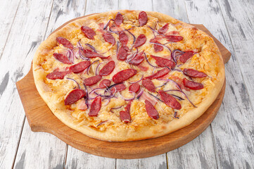 Texas pizza with smoked sausages, red onion and mozzarella cheese. Round wooden board. Light wooden background. View from above.