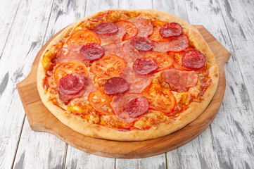 Pizza with ham, salami, tomato sauce and mozzarella cheese. Round wooden board. Light wooden background. View from above.