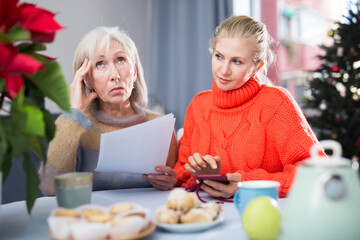 Mature woman and her adult daughter, who came to visit her before Christmas, study an important...