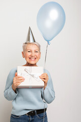 Amazed elderly woman holding blue balloon and gift box
