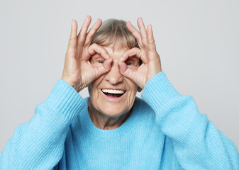 Old grey-haired woman smiling happy doing ok sign with hands on eyes