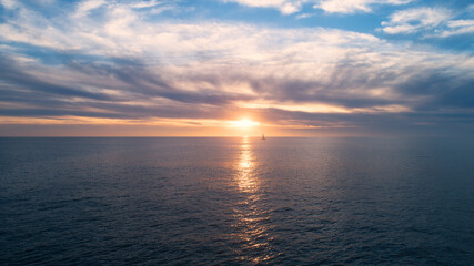 Sunset on the horizon of the Pacific Ocean with Sailboat crossing the reflective glow of the sun