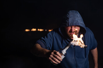 The man in the hood is holding a burning bottle. Molotov cocktail.