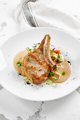 Roasted pork steak with vegetables garnish and sauce. Bone-in ribeye pork chops. Main course of pork in rustic style.
