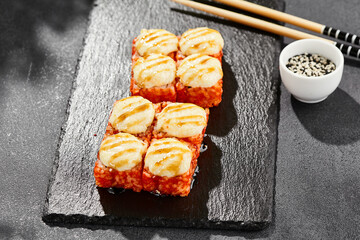 Baked Maki sushi on dark slate. Hot california maki with cheese. Sushi roll with tobiko outside, baked cheese topped. Style concept japanese menu with black background, leaves and hard shadow.