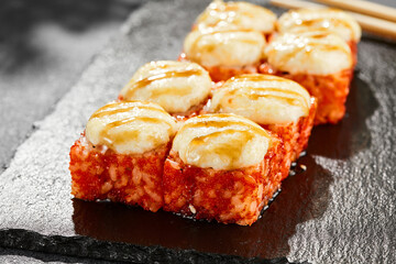 Baked Maki sushi on dark slate. Hot california maki with cheese. Sushi roll with tobiko outside, baked cheese topped. Style concept japanese menu with black background, leaves and hard shadow.