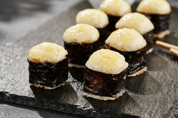 Baked Maki sushi on dark slate. Hot cheese hosomaki roll. Simple sushi roll with cheese, baked cheese topped. Style concept japanese menu with black background, leaves and hard shadow.