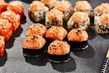 Hot maki set on dark slate. Baked sushi set with hot rolls. Sushi rolls with salmon,tobiko and baked cheese topped. Style concept sushi menu with black background, leaves and hard shadow.