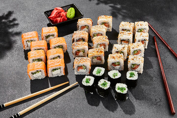 Maki sushi set on dark background. Maki set with variety rolls. Composition from popular sushi rolls and hosomaki. Style concept sushi menu with black background, leaves and hard shadow.
